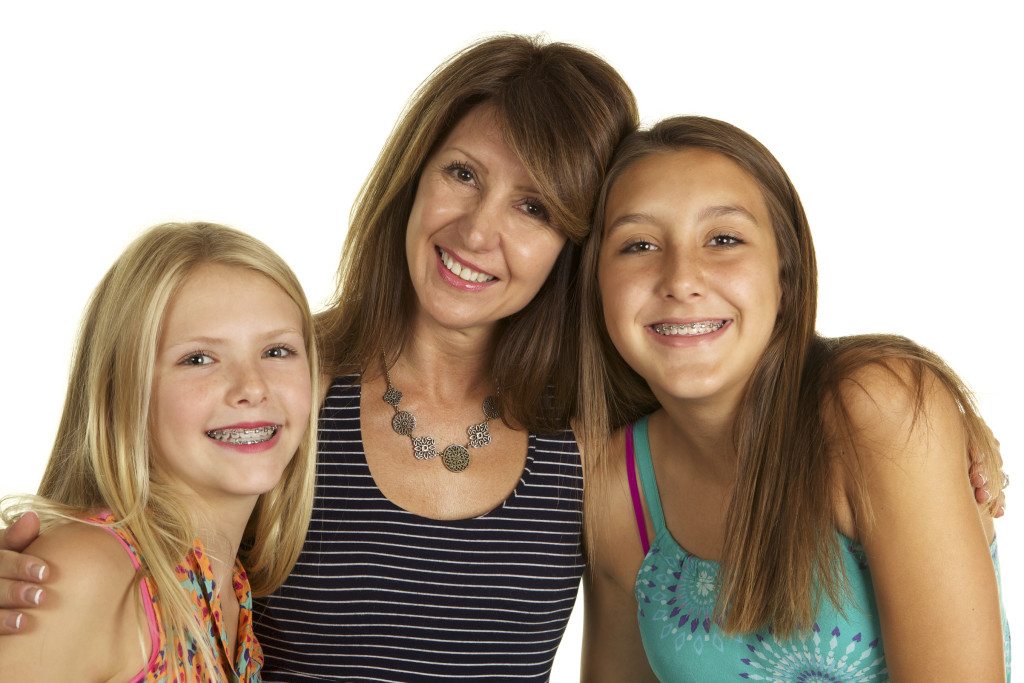 A beautiful mom in her fifties and her daughters, ages ten and thirteen smiling at the camera on a white background.