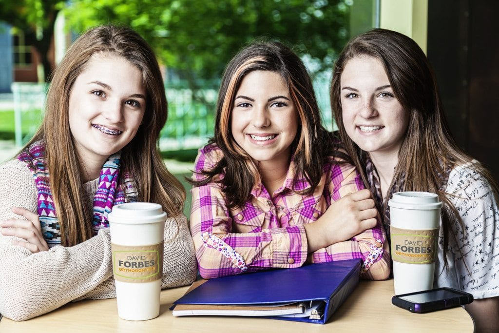 Three smiling girls sitting at a cafe table.